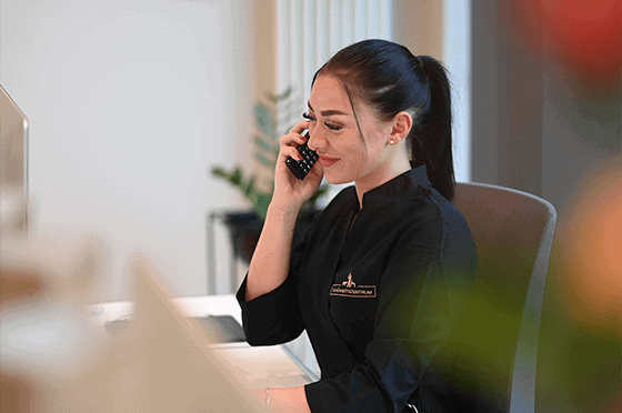 Mitarbeiterin eines Schönheitszentrums nimmt freundlich einen Anruf am Empfang entgegen, trägt schwarze Dienstkleidung und sitzt an einem modernen Schreibtisch.