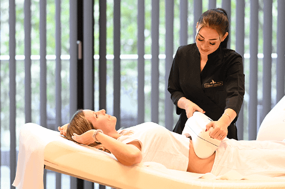 Kundin liegt entspannt auf einer Behandlungsliege, während eine Fachkraft ein Kryolipolyse-Gerät zur gezielten Fettreduktion am Bauch anwendet.